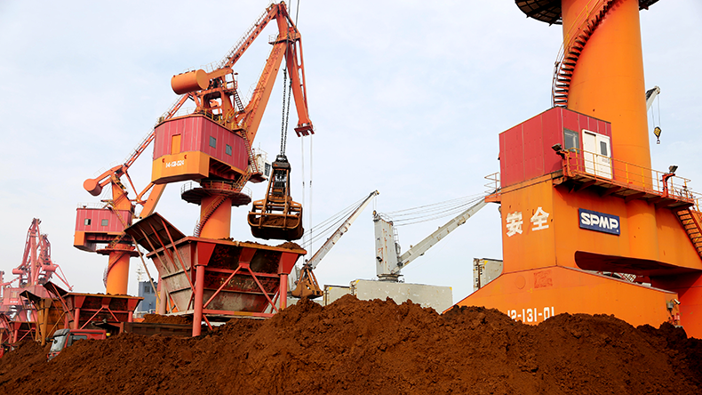 Grab bucket cranes along a quay unload iron ore from a bulk ship at Lianyungang port