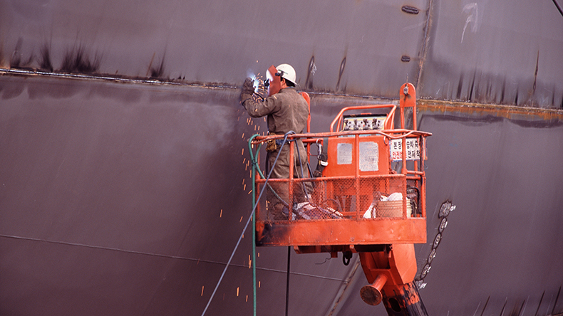 Worker welding hull section of new containership in Pusan, South Korea 