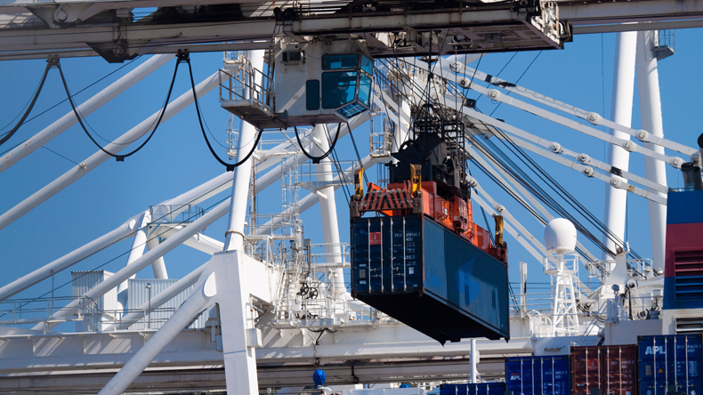 Crane lifting container off ship with blue sky